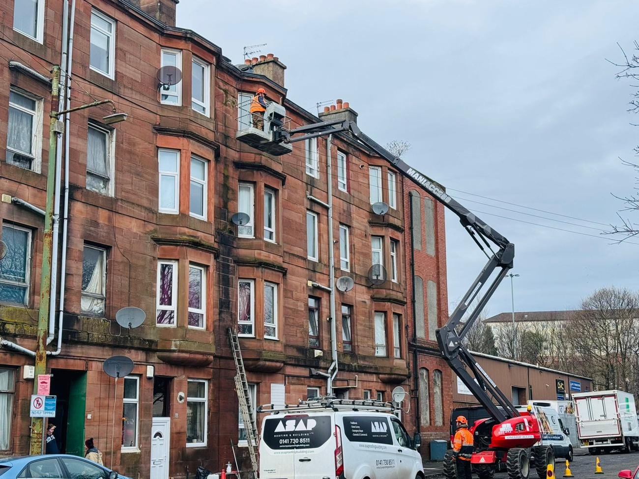 Cherry picker lifting a roofer to the eaves of a red sandstone tenement
